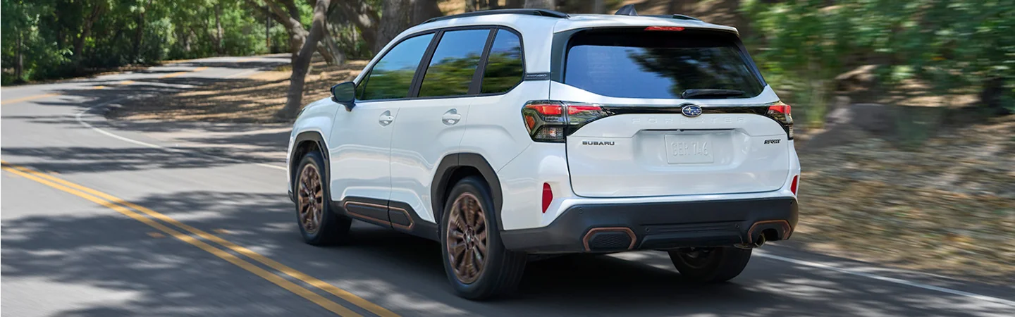 Back side view of a gold 2025 Subaru Forester driving in a neighborhood in Nederland, TX