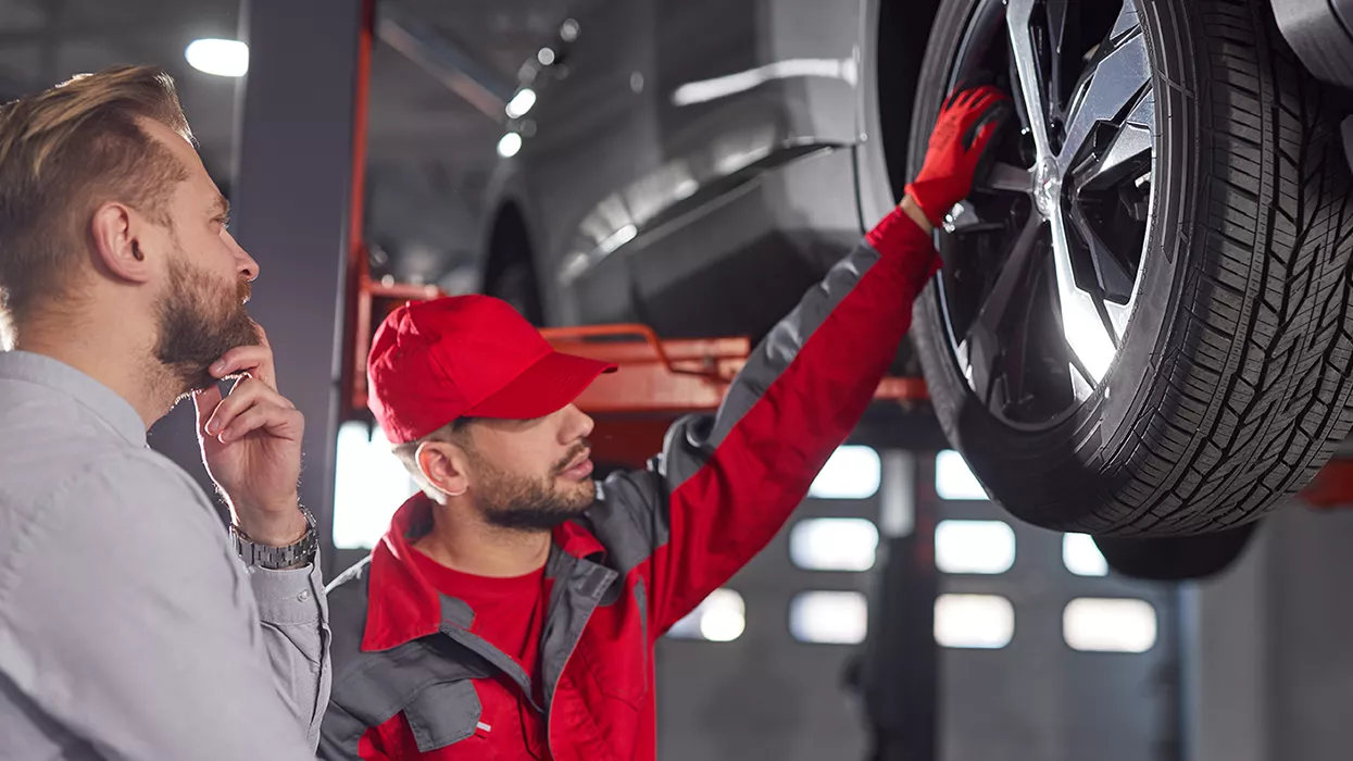 Service mechanic standing next to a lifted car