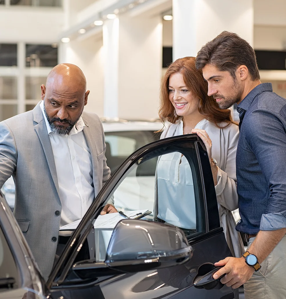 Sales person showing customers around a new car