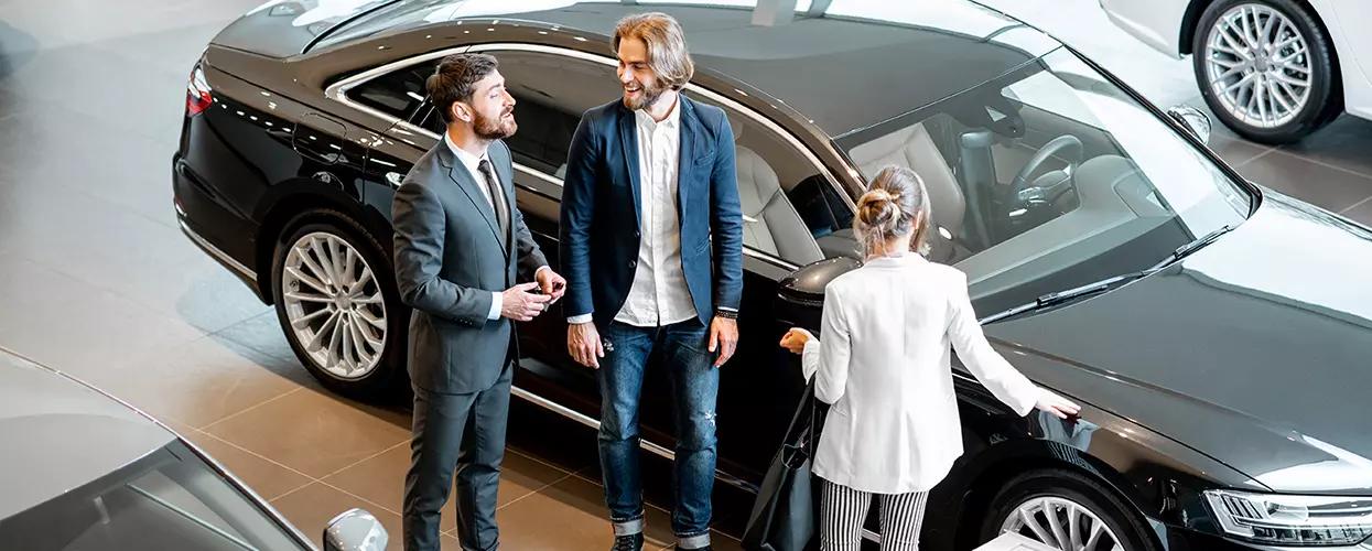Car dealership sales consultant assisting customers while exploring a luxury sedan in a modern showroom
