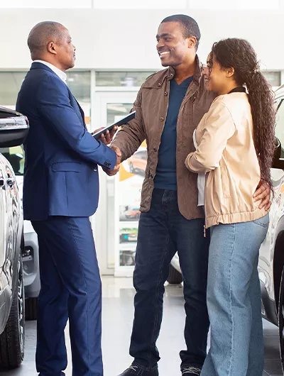 one person shaking hand of another with another person stand along side after a good car sale interaction