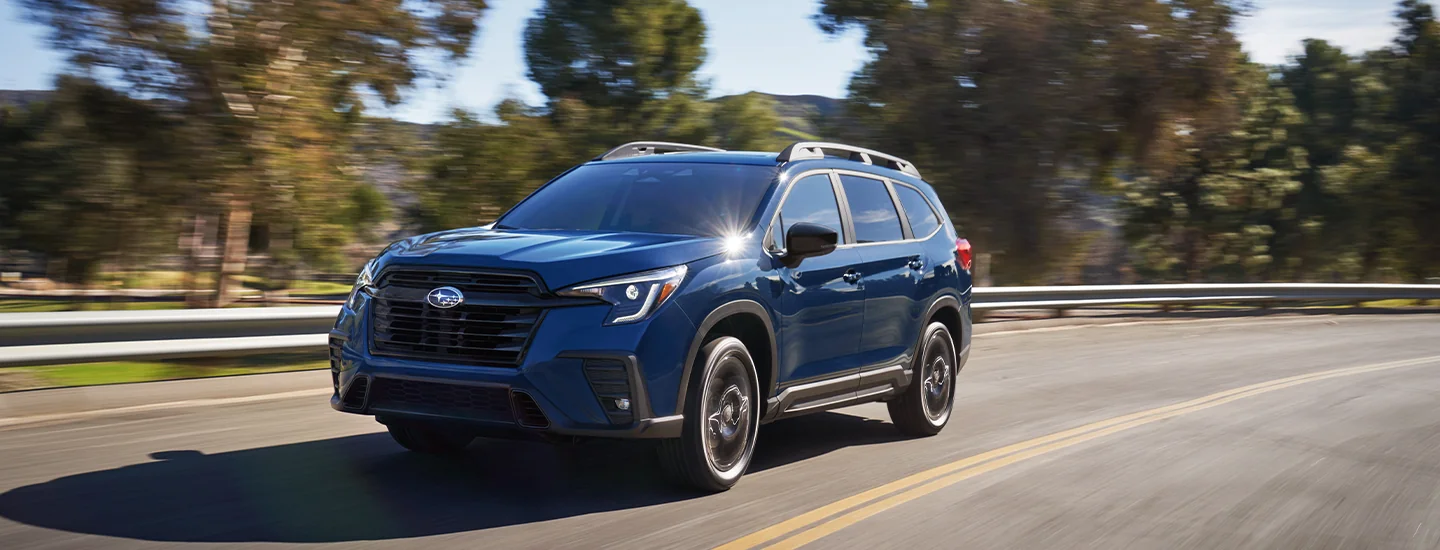 Front view of a blue 2026 Subaru Ascent driving on a tree lined road