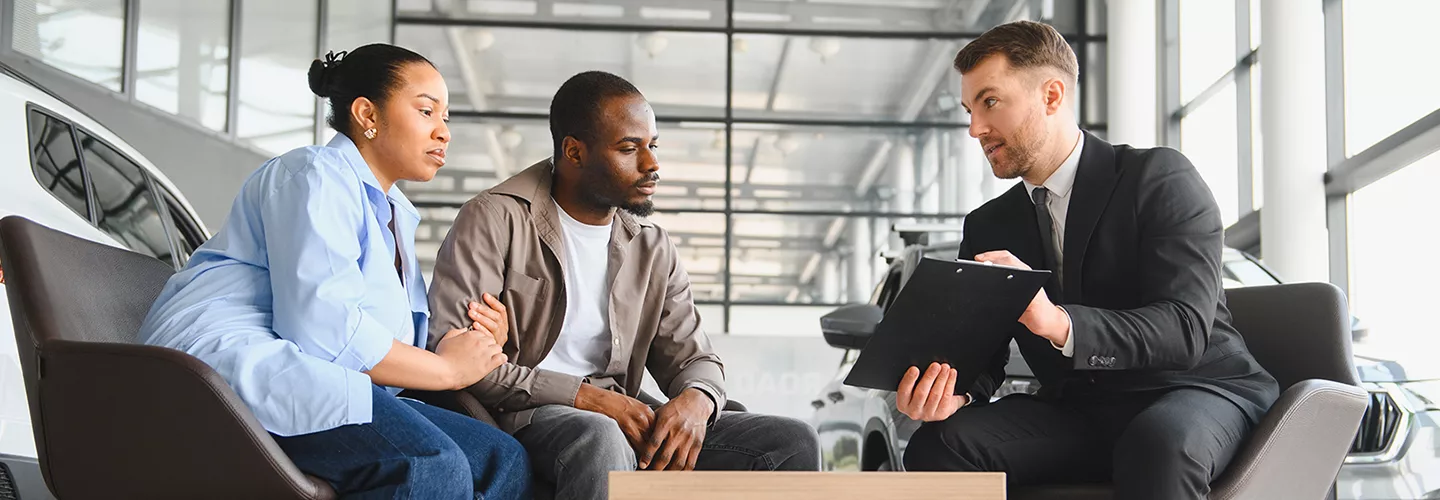Car salesman talking with a couple and showing them a clipboard