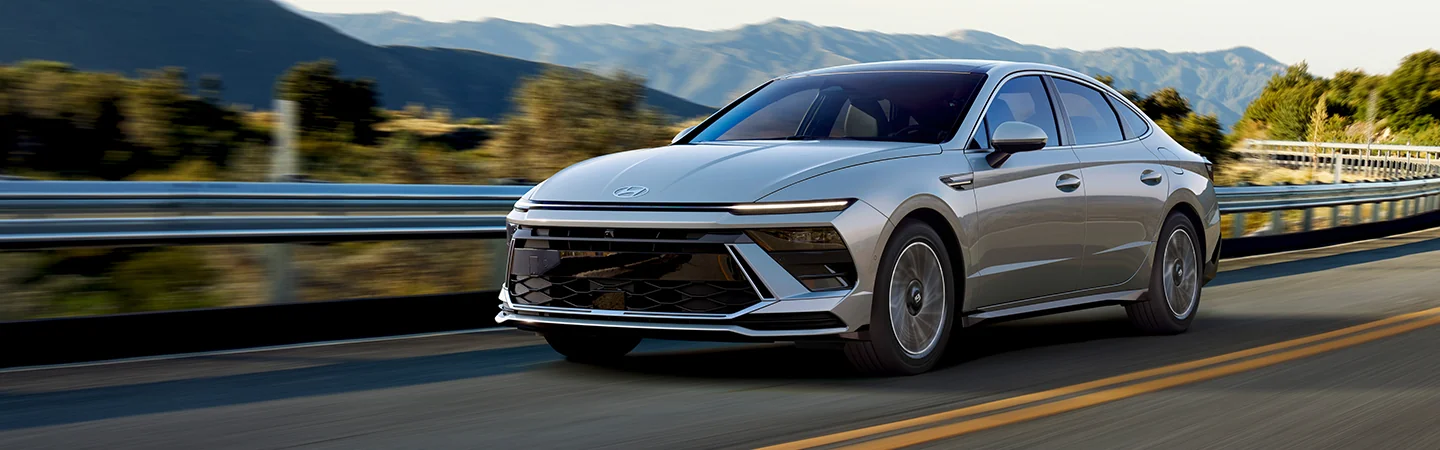 A gray 2025 Hyundai Sonata driving on a road with mountains in the background