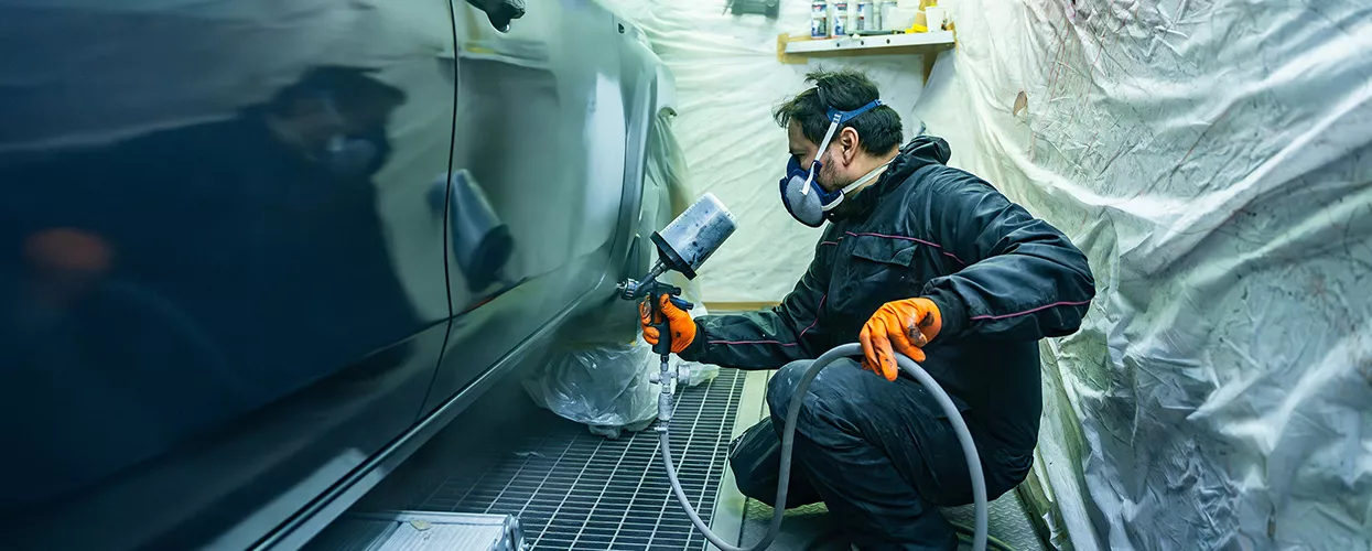 Automotive body shop technician applying paint to a vehicle during collision repair and refinishing service