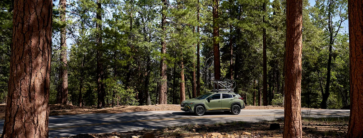 2026 Subaru Crosstrek driving through a wooded area with bikes on the roof racks