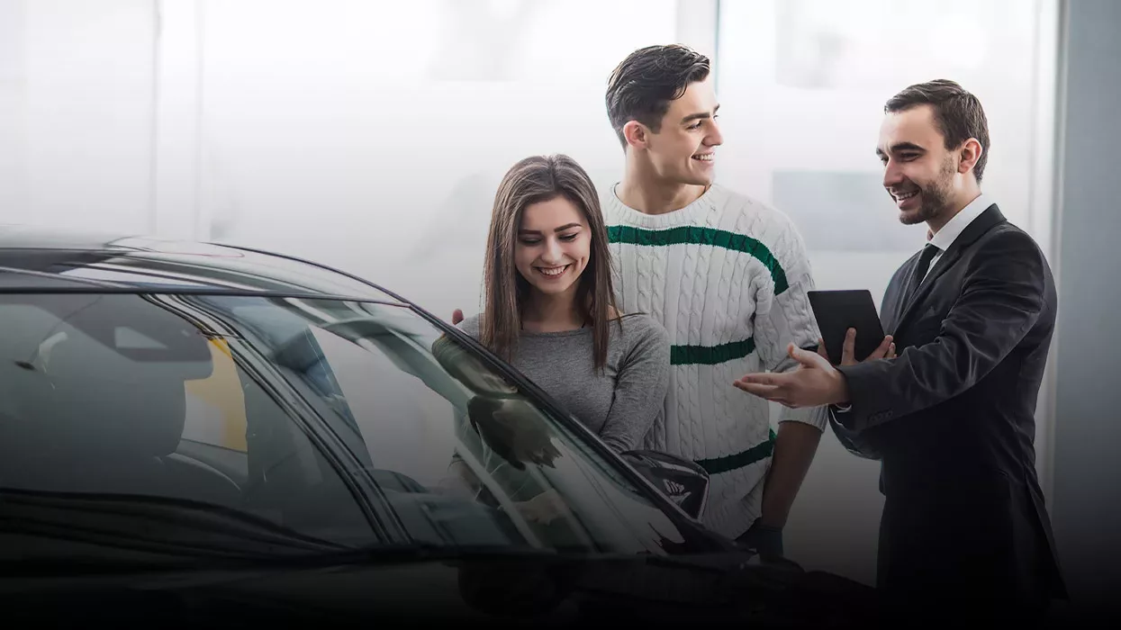 salesman showing a car to a man and woman