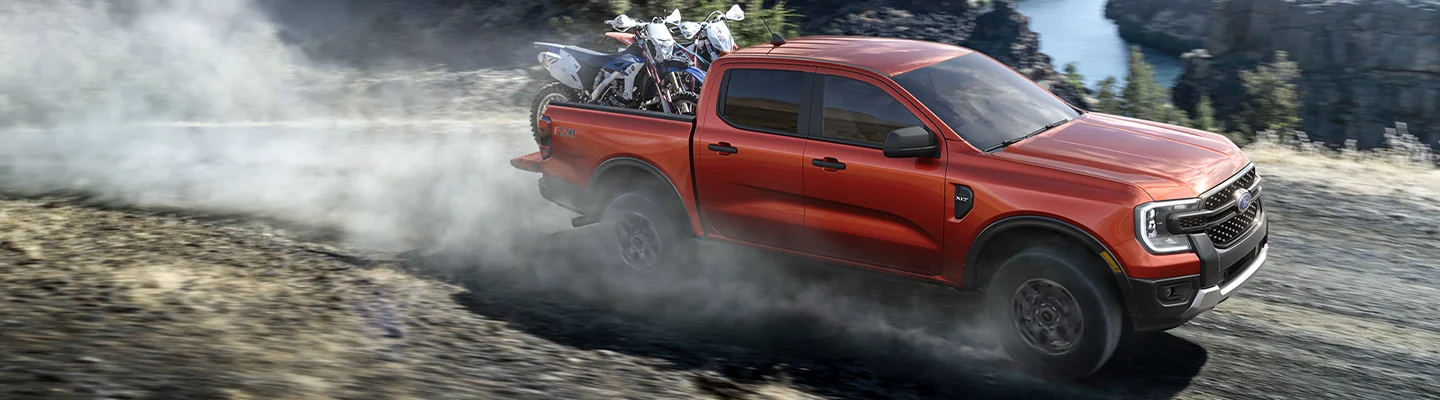 A 2025 Ford Ranger driving on a dirt road with dirt bikes in the back