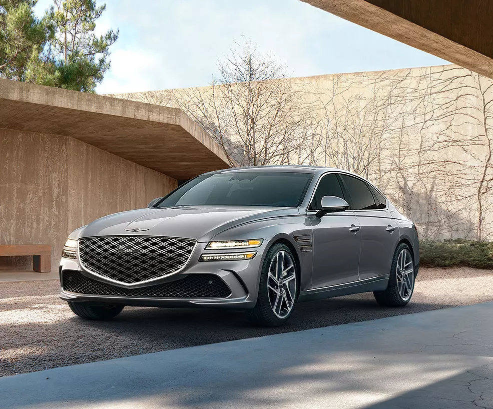 Front view of a gray 2027 Genesis G80 parked in a rocky driveway