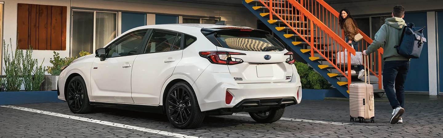 Back view of a white 2026 Subaru Impreza parked at a motel with a family heading in