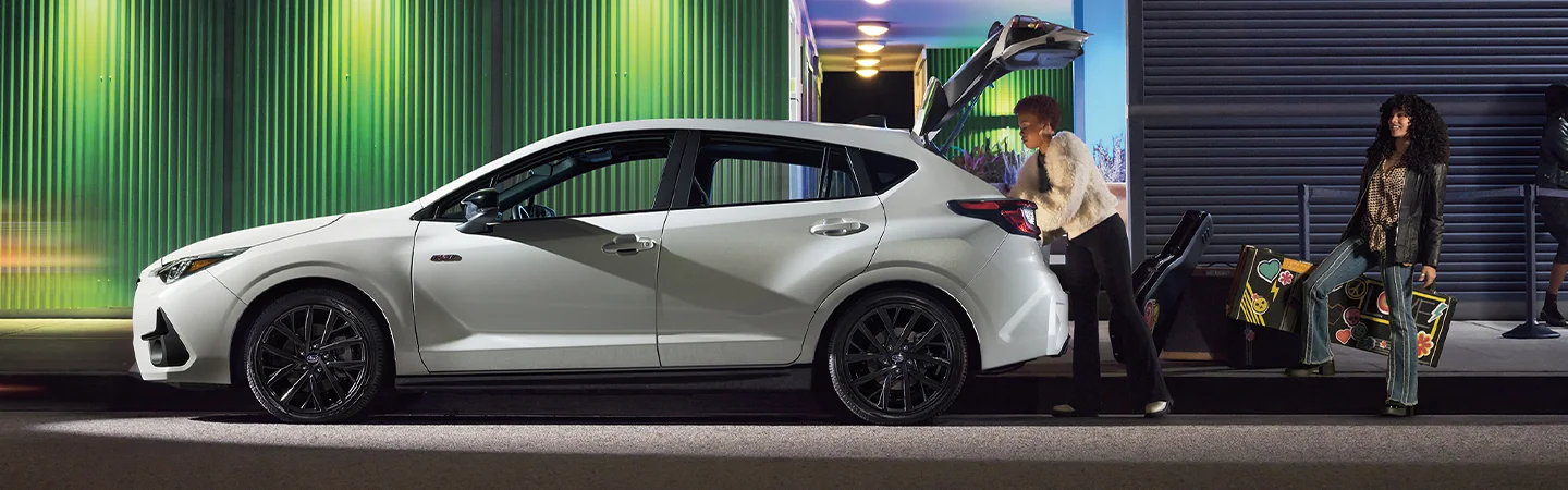 Side view of a parked white 2026 Subaru Impreza in the city with a band louding up band equipment
