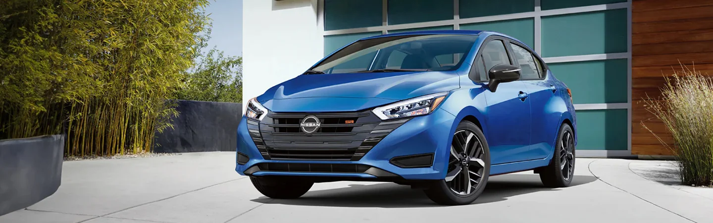 A blue 2024 Nissan Versa Specs parked in a driveway