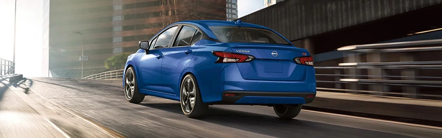 Back view of a blue 2024 Nissan Versa driving in the city