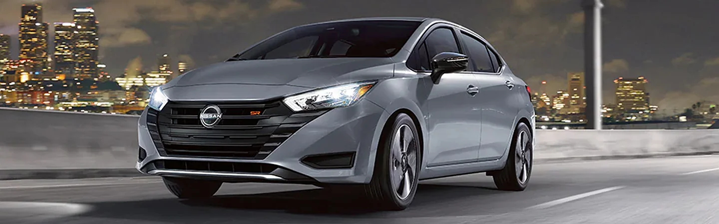 A gray 2024 Nissan Versa driving on a freeway with a city in the background