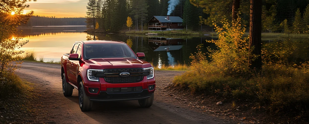 Front view of a red 2026 Ford Ranger parked by a lake with a cabin on it