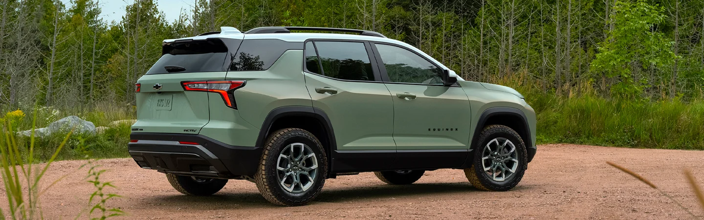 Back side view of a green 2025 Chevrolet Equinox parked next to the woods