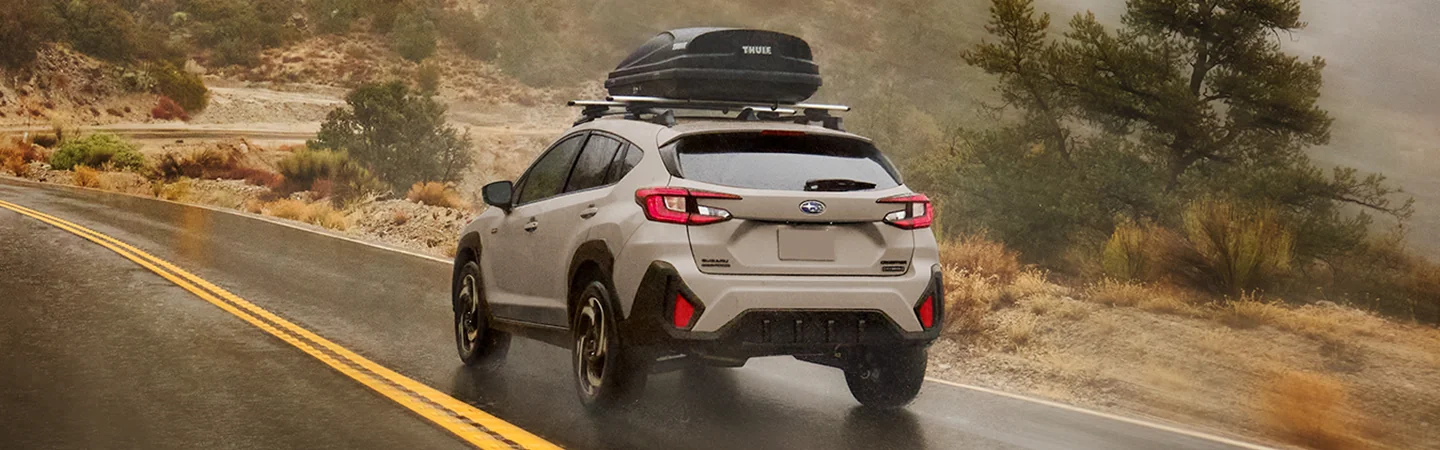 rear view of a white 2026 Subaru Crosstrek Hybrid Sport driving in rain