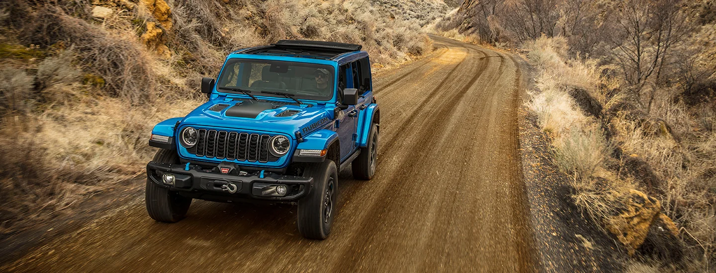 Blue 2025 Jeep Wrangler driving on a dirt road