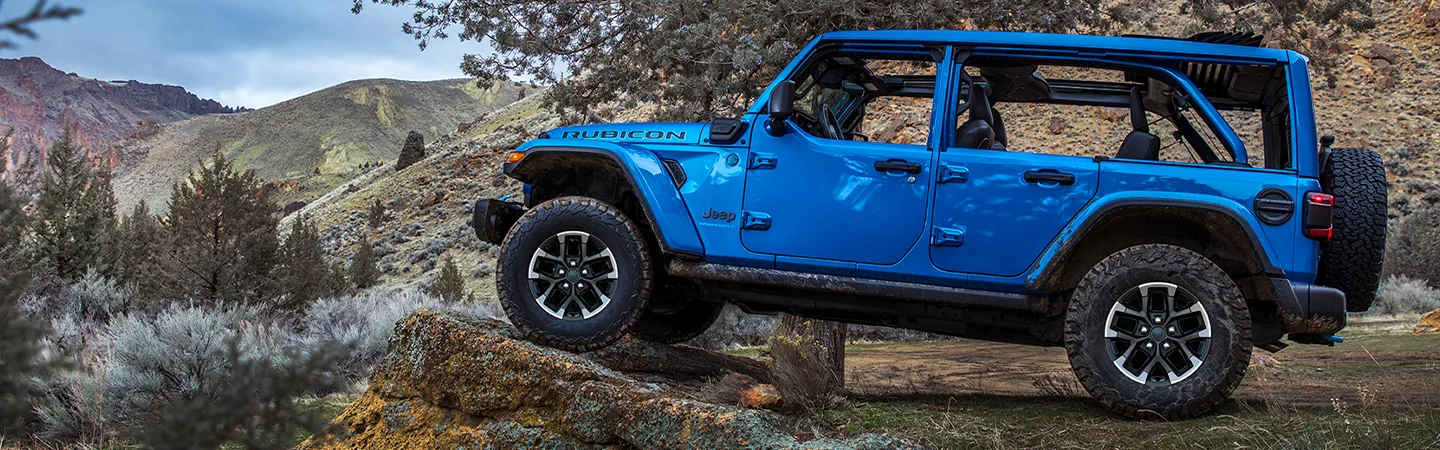 Side view of a parked blue 2025 Jeep Wrangler in the wilderness