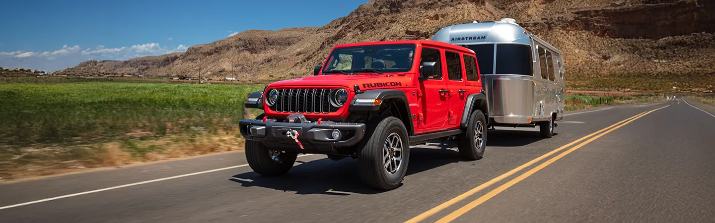 Red 2025 Jeep Wrangler towing a camper