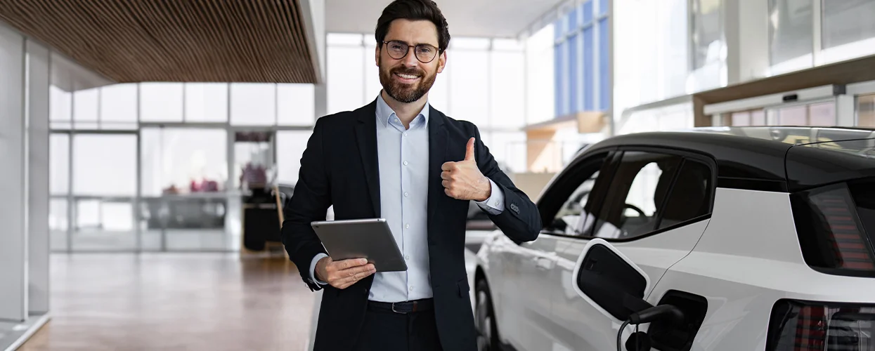 A suited man displays a tablet in front of a luxury car, indicating a business or automotive context.