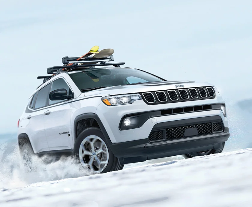 Front side viewe of a white 2026 Jeep Compass driving in the snow