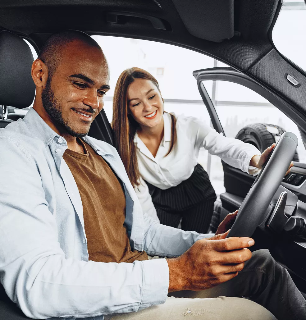 Person sitting in a new vehicle with a car sales woman standing outside