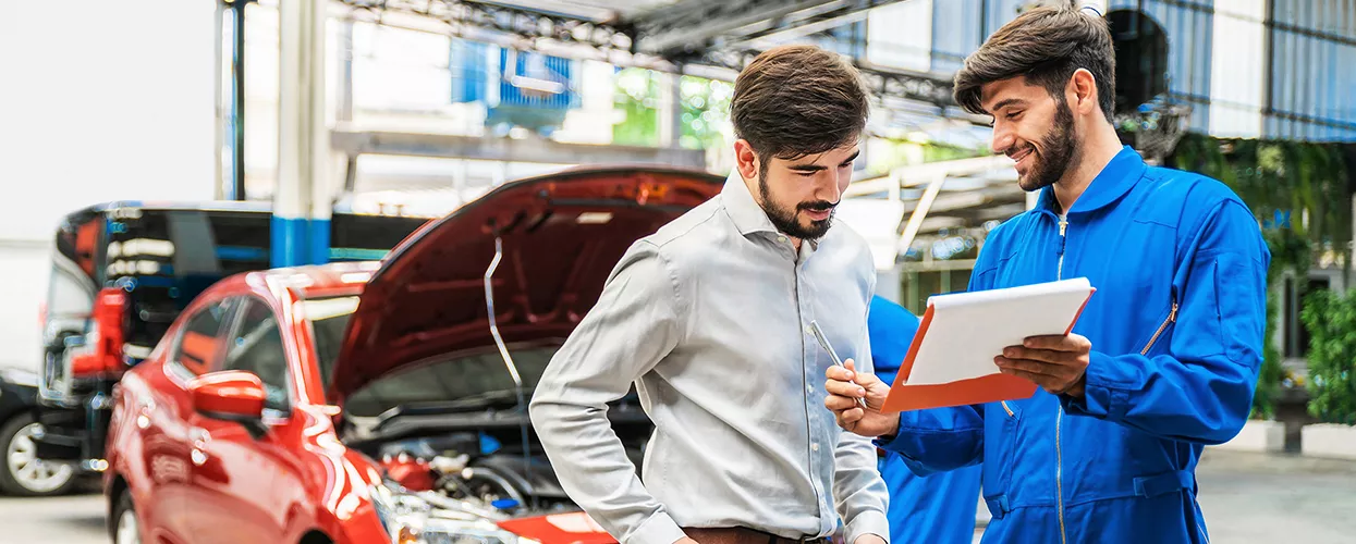Service mechanic showing a car owner a clipboard with a car in the background