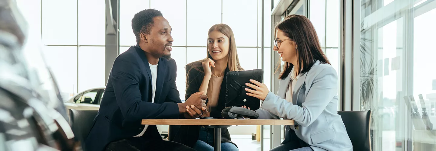 saleswoman with man and woman in the dealership looking over a tablet