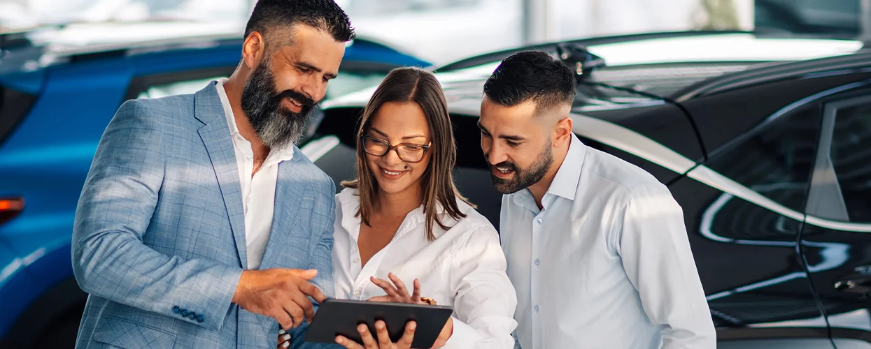 couple being shown details of car financing with car salesman in showrooom on pad computer