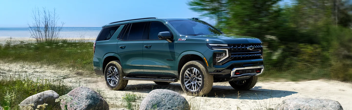 Side view of a green 2025 Chevrolet Tahoe driving by the beach