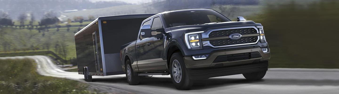 A black 2021 Ford F-150 towing a trailer up hill