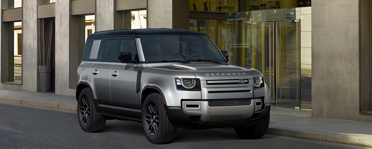 A silver Land Rover Defender 110 parked in front of a modern building, showcasing its sleek design against the urban backdrop.