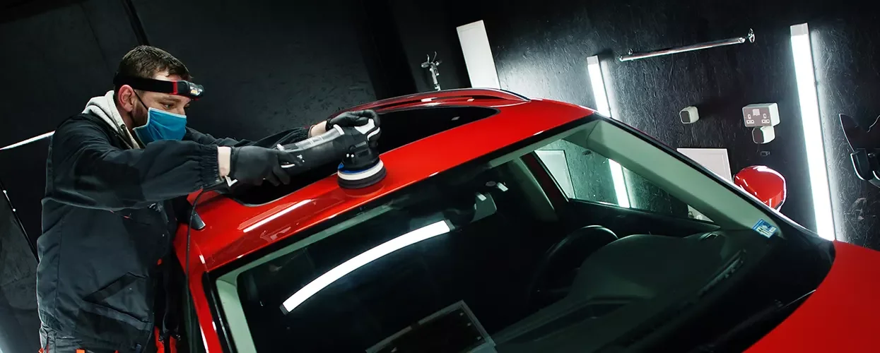 Collision service tech working on buffing the roof of a red car