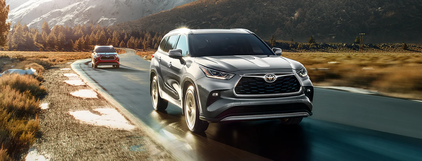 2025 Toyota Highlander driving down a country road with sunlight in the background