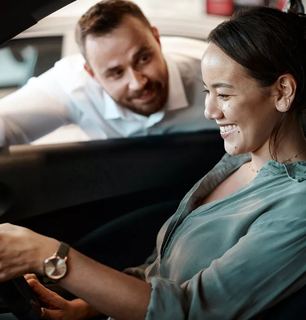 Woman sitting in a new car with a car salesman standing outside