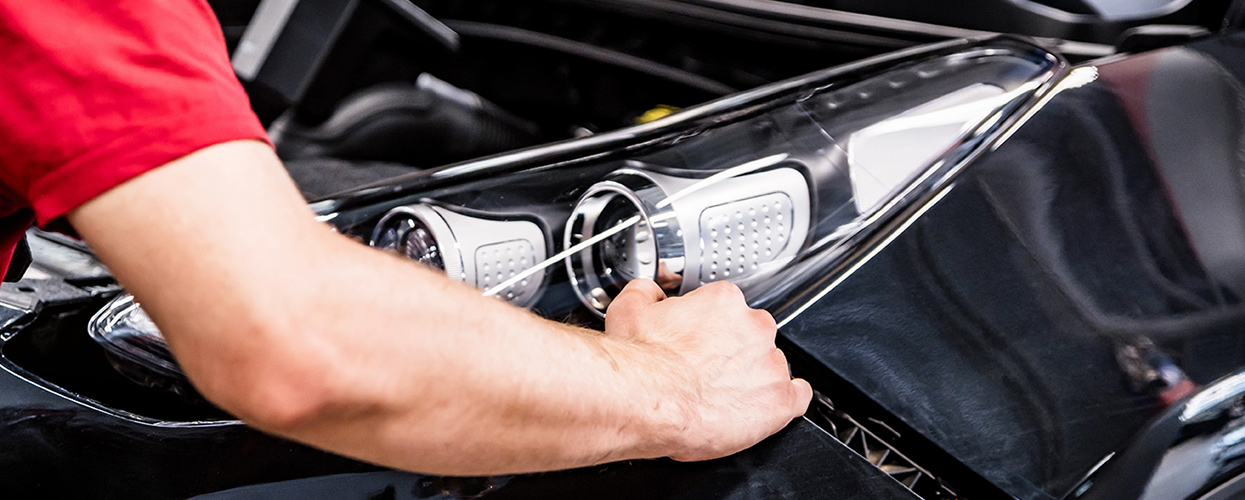 A man repairing a car, focused on the task with tools in hand and the vehicle's hood raised.