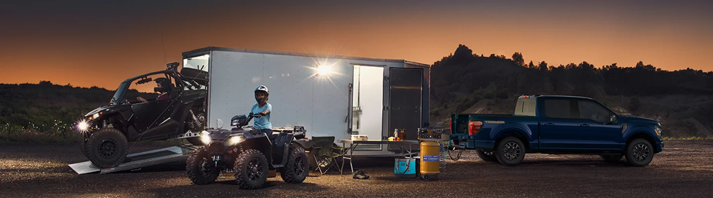 Ford Truck with a trailer, ATV, and UTV in front of some hills