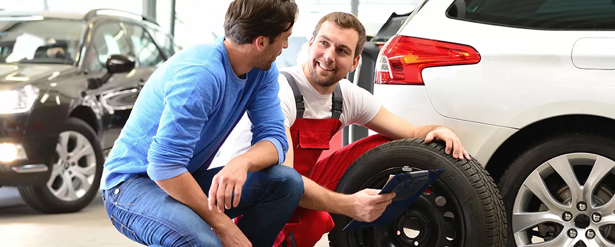 Service mechanic changing a vehicles tires and talking to a customer
