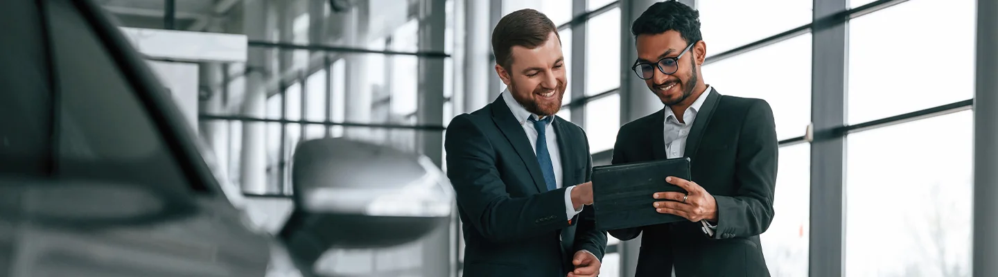 two guys in a dealership looking a tablet next to a vehicle
