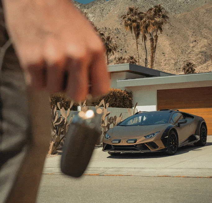 A person grips a remote control, positioned in front of a vehicle.