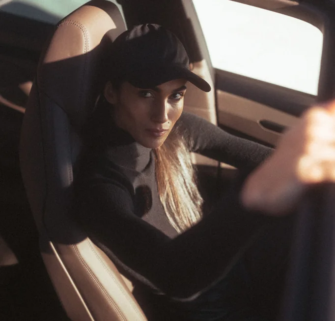A woman with a hat is positioned in the driver's seat of a car, looking forward.
