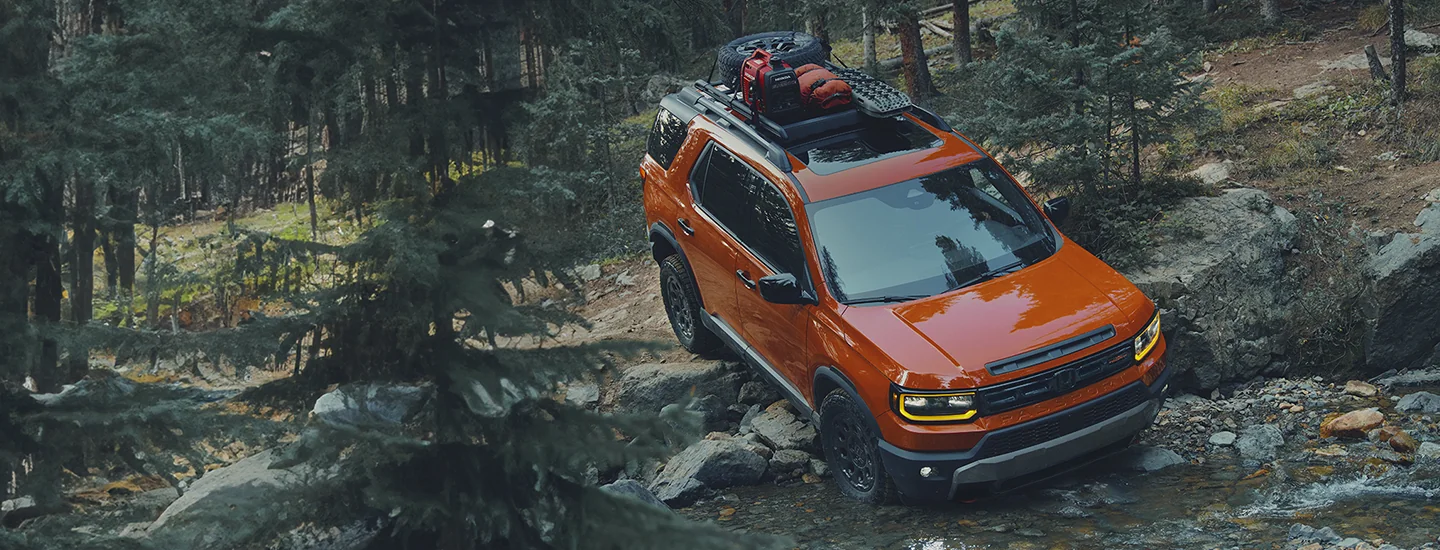 Orange 2026 Honda Passport driving in the woods though a river