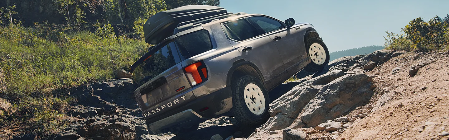 Side view of a gray 2026 Honda Passport driving up a rocky hill side