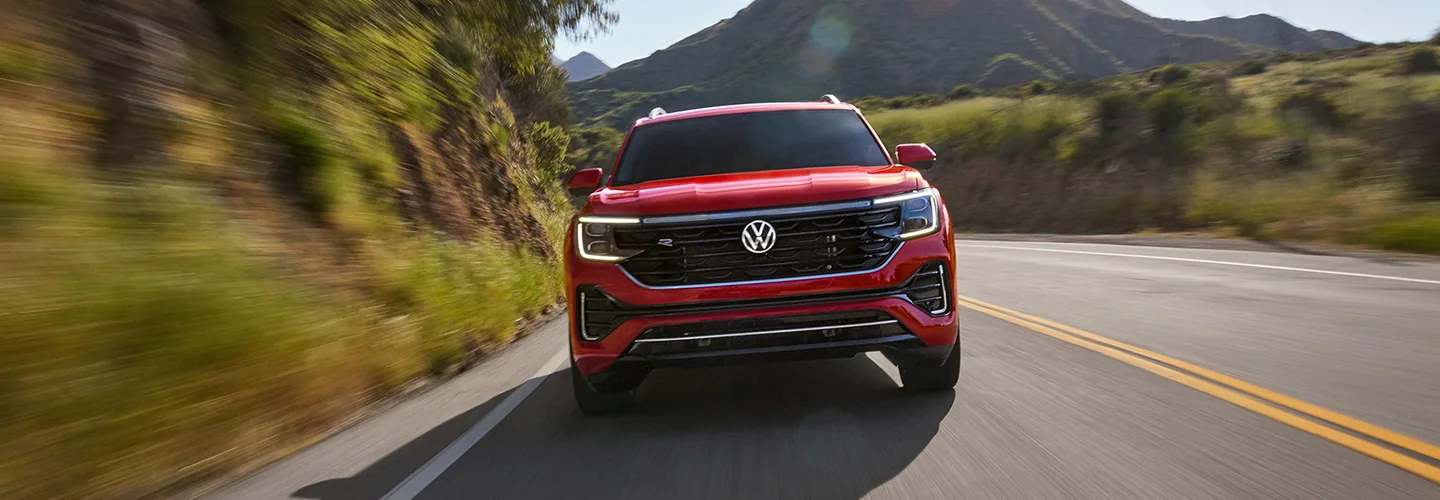 Front view of a red Volkswagen Atlas driving on a road next to some mountains