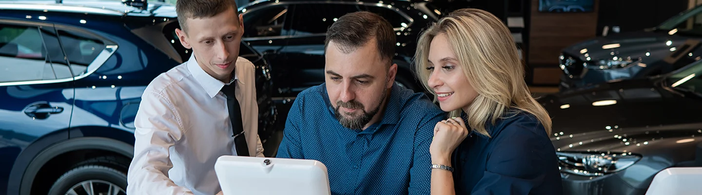two people looking at details of car purchase with another in showroom