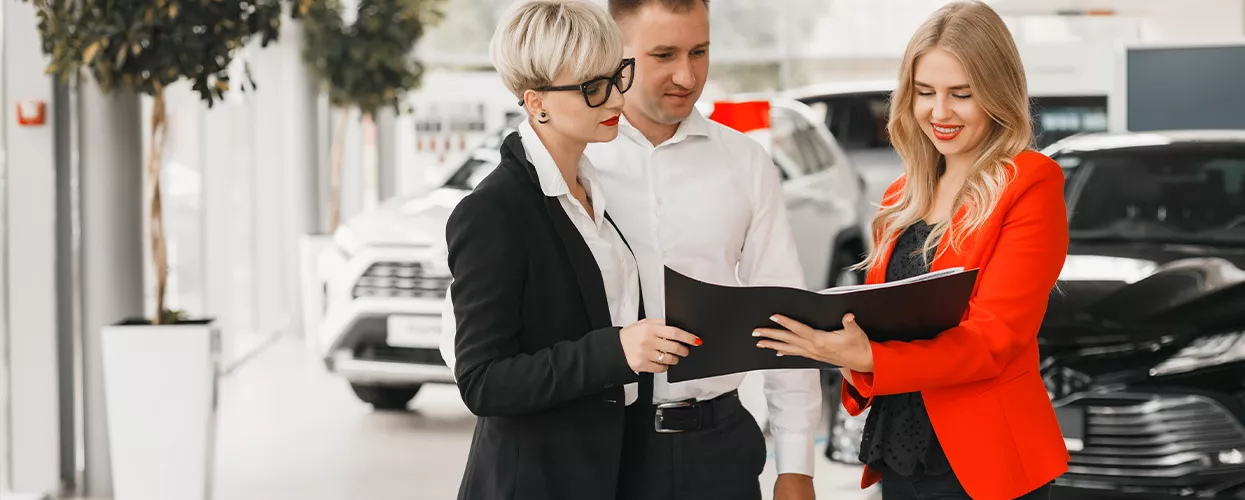 Three people looking at a document in a dealership