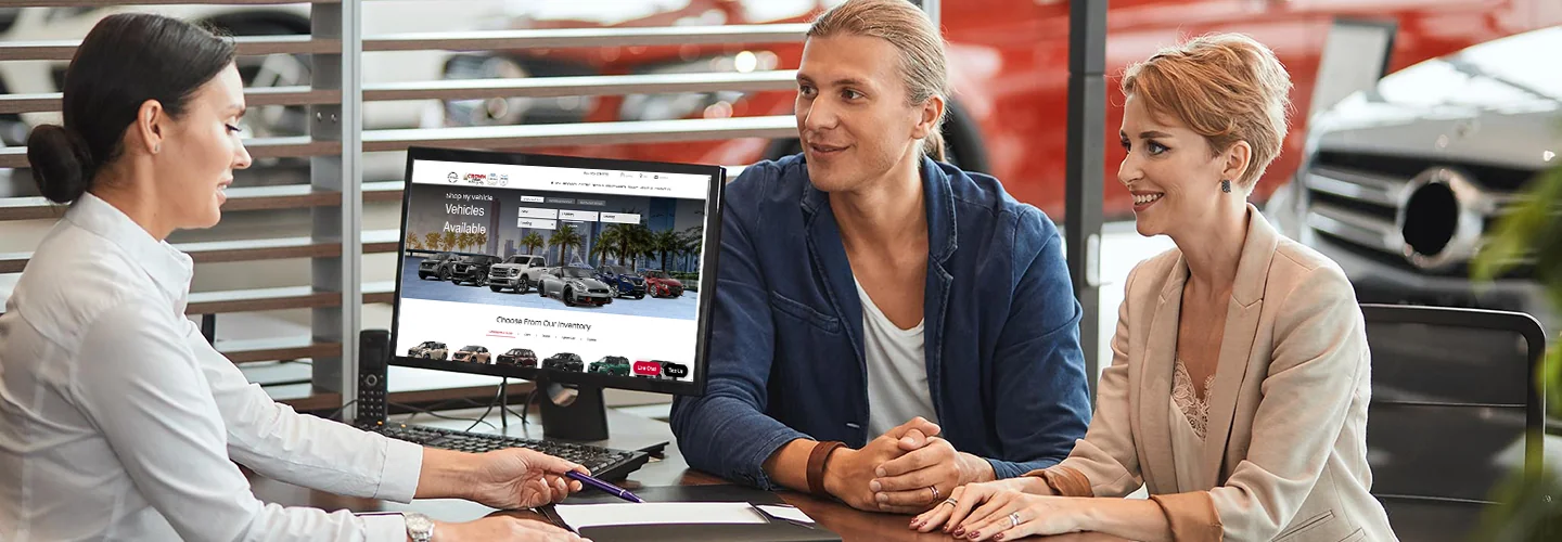 two people speaking with another person behind a desk in the car dealership