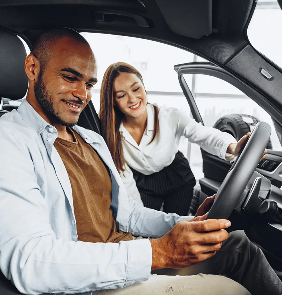 saleswoman reaching into the vehicle with man sitting in the driver seat