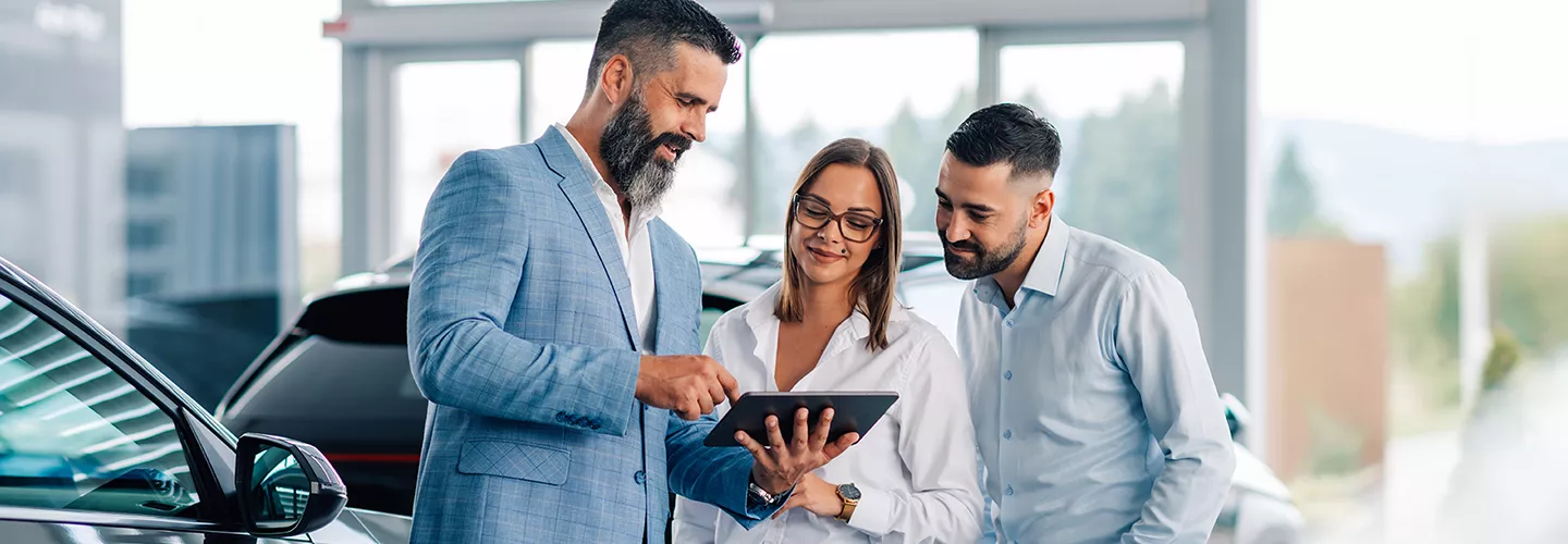 Car salesman showing a couple something on a tablet, in a car dealership